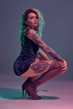 Mavi kadife şort ve kestane rengi süet çizmeler giyen genç, güzel, sarışın kadın, bazı twerk hareketler gösteriyor, baştan çıkarıcı görünüyor..