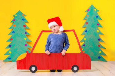 Çocuk Noel şapka karton bir araba ile. Küçük kız evde sarı bir arka plan üzerinde eğleniyor. Noel kavramı. Yeni yıl tatilleri.