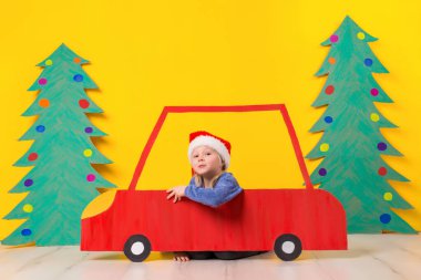 Kırmızı Noel araba çocuk. Boyalı araba ve yeşil Noel ağacı karton sarı bir arka plan üzerinde yapılmış. Xmas tatil kavramı. Küçük duygusal kız