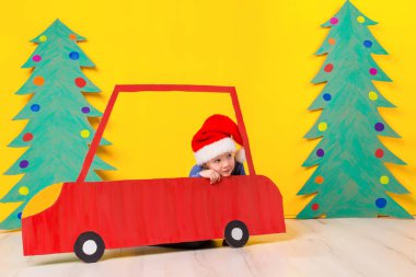 Kırmızı Noel araba çocuk. Boyalı araba ve yeşil Noel ağacı karton sarı bir arka plan üzerinde yapılmış. Xmas tatil kavramı. Küçük duygusal kız