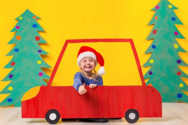 Çocuk Noel şapka karton bir araba ile. Küçük kız evde sarı bir arka plan üzerinde eğleniyor. Noel kavramı. Yeni yıl tatilleri.
