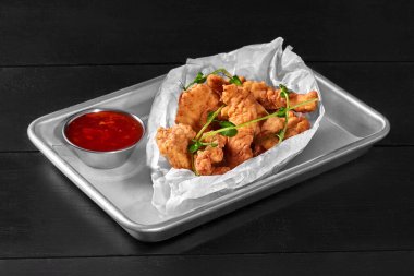 Baharatlı, bol yağda kızartılmış tavuk fileto hamuru metal tepside servis edilir ve taze mikroyeşilliklerle süslenir. Amerikan tarzı atıştırmalık