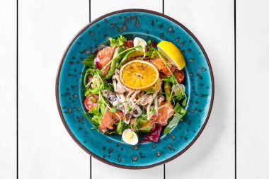 Yeşillik, avokado, bıldırcın yumurtası, kiraz domatesleri, mürekkep balığı, midye ve taze limon ve kurutulmuş portakal dilimiyle süslenmiş hafif soslu tuzlu somon balığı salatası.