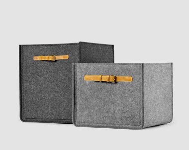 İki el yapımı gri keçeli kutu farklı boyutlarda ve beyaz arka planda kum renkli deri sapları var. Ev alanı düzenlemek ve eşyaları depolamak için şık aksesuarlar