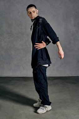 Dövmeli, küpeli, sakallı atletik adam. Beyaz tişört, spor ayakkabı, siyah kot gömlek ve pantolon giymişti. Gri arka planda dans etmek. Dans salonu, hip-hop. Tam uzunluk, boşluğu kopyala