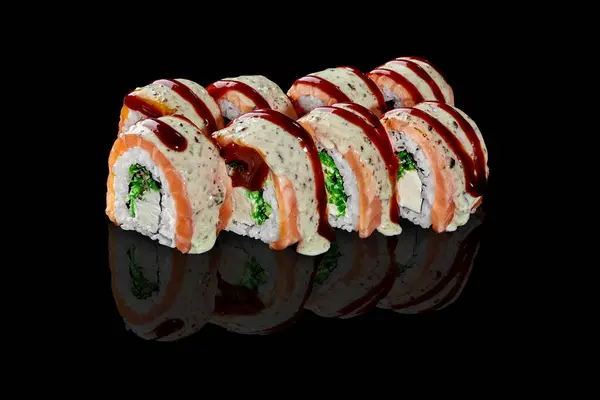 Closeup of delicious sushi rolls filled with cream cheese and hiyashi wakame wrapped in salmon fillet, topped with peanut sauce and savory unagi sauce, presented on black reflected surface