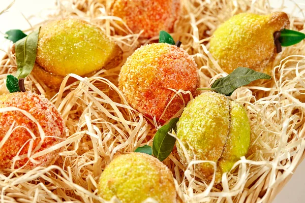 Variety of colorful shortcrust pastry cookies in shaped of fruits dusted with sugar arranged in natural straw basket, evoking summer harvest bounty