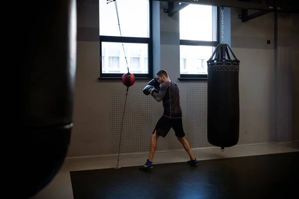 Determined adult man in sportswear and boxing gloves training with floor to ceiling bag, strengthening muscles, improving reflexes and punching speed in gym setting