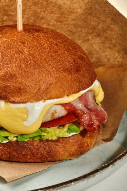 Kızarmış pastırma dilimleri, domates, avokado ve tabağa sarılmış kremalı peynir soslu tavuk burger. Popüler fast food konsepti