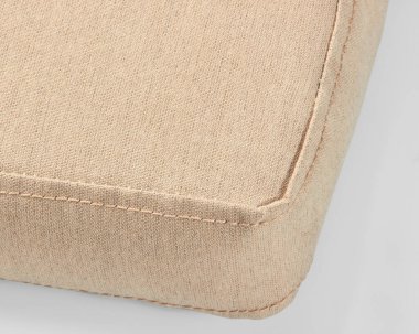 Bej renkli keten yastık köşesinin yakın çekimi, temiz beyaz arkaplan üzerindeki dikişleri vurguluyor.