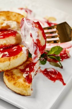 Çilek reçeli, ekşi krema ve bademle kaplanmış lezzetli şurup, altın çatalla tatlandırılıyor.