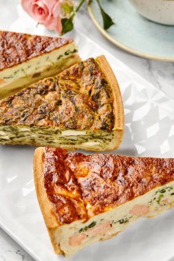 Çeşitli dolgularla ev yapımı kiş dilimleri beyaz bir tabakta görsel olarak çekici bir düzen oluşturuyor.