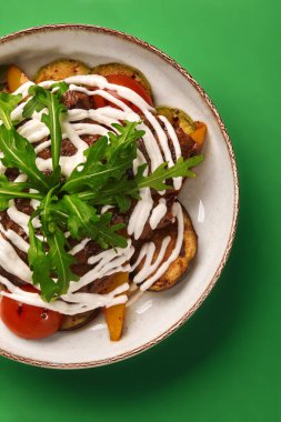 Lezzetli ızgara kuzu ızgara sebze, roka ve yoğurt sosu yeşil arka planda servis edilir.