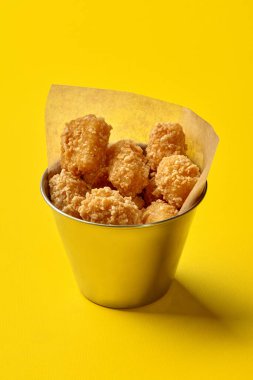 Patates kroketleri canlı sarı bir arka planda metal bir kovaya taşarak görsel olarak çekici bir fast food sahnesi yaratıyor.