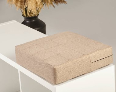 Rahat bir bej yastık beyaz bir bankta, rahat ve davetkar bir oturma alanı yaratıyor.