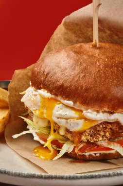 Lezzetli hamburger, kızarmış yumurta, erimiş peynir, marul, domates ve damlayan sarısı, tabakta patates kızartması ile servis ediliyor.