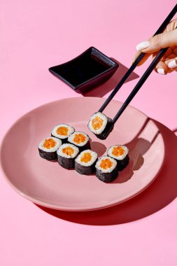 Siyah çubuklu el soya soslu pembe tabaktan soya soslu somon uramaki suşi rulosu topluyor.
