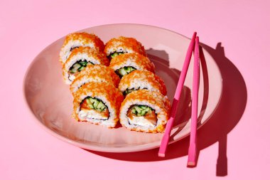 Somon, krem peynir, salatalık ve tobiko havyarlı suşi, pembe yemek çubuklarıyla servis edilen pembe bir tabakta servis ediliyor.