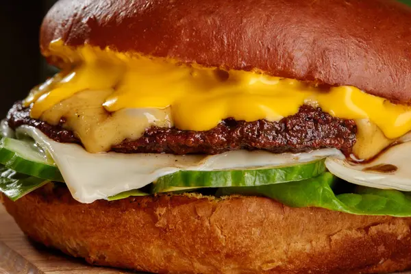 Erimiş çedar peyniri, taze turşu ve kızarmış brioche çöreği arasında gevrek marul kaynayan sulu bir çizburgerin yakın çekimi.