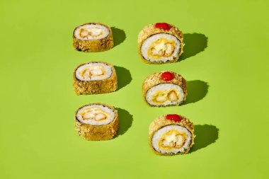 Lezzetli tempura maki suşi sarmaları canlı yeşil bir arka planda sunulur, görsel olarak çekici bir mutfak sahnesi yaratır.