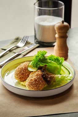 Tavuklu kiev pirzolası patates püresi, salatalık ve marulla servis edilir. Lezzetli ve görsel olarak çekici bir yemek olur.