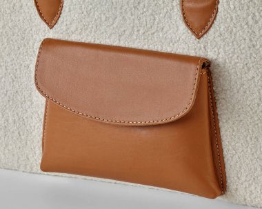 Krem şerpa çantasındaki kahverengi deri bir cebin yakın çekimi, moda ve tasarım ayrıntılarını gösteriyor.