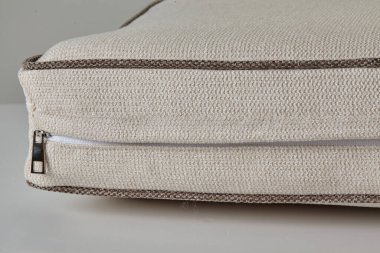 Beyaz arka planda kapalı fermuar içeren kahverengi borular içeren bej yastık kapağı.