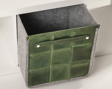 Yeşil deri bir depo kutusu beyaz bir raftan çıkartılıyor ve şık bir depolama çözümü sunuyor.