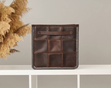 Küçük saplı ve gri keçeli kalemle kahverengi deri düzenleyici beyaz rafta oturup zarif bir depolama çözümü sunuyor.