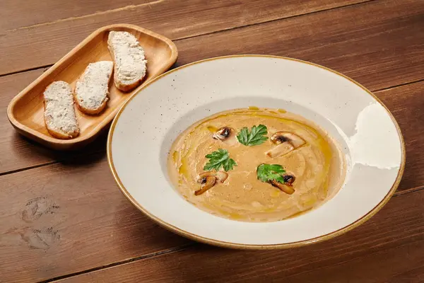 Kızarmış ekmek dilimleriyle servis edilen mantar kremalı çorba maydanoz ve mantarla süslenmiş.