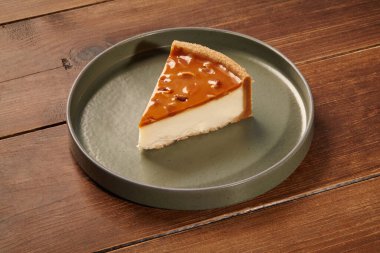 Kremalı peynirli kek, karamelli ve fındıklı, yeşil seramik tabakta, ahşap bir masanın üzerinde servis ediliyor.