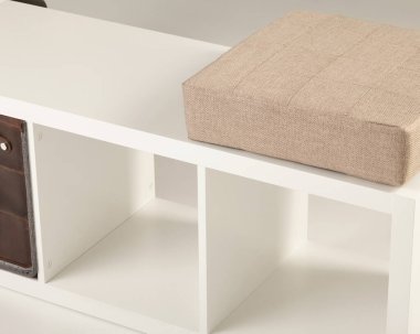 Rahat bir bej yastık ve boş kompartımanlar içeren şık beyaz depolama tezgahı, herhangi bir yaşam alanını düzenlemek için mükemmel.
