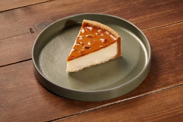 Kremalı peynirli kek, karamelli ve fındıklı, yeşil seramik tabakta, ahşap bir masanın üzerinde servis ediliyor.
