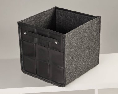 Modern depolama kutusu keçeyle deriyi birleştiriyor, beyaz bir raftaki eşyaları düzenlemek için şık bir çözüm sunuyor.