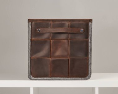 Gri keçeli ve saplı kahverengi deri bir kutu beyaz rafta dinleniyor ve şık bir organizasyon sunuyor.