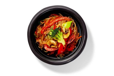 Lezzetli selofan erişteler, renkli sebzeler ve mantarlarla kızartılmış, siyah bir kasede servis ediliyor.