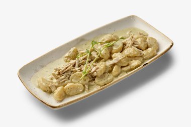 Dikdörtgen bir tabakta servis edilen tavuk, kremalı sos ve bezelye filizi ile nefis bir gnocchi çok cazip bir mutfak deneyimi sunuyor.