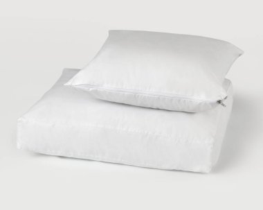 Beyaz arka planda fermuarlı beyaz yastık ve yatak koruyucusu. Uyku sırasında hijyen ve konforu teşvik ediyor.