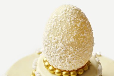 Hindistan ceviziyle kaplı beyaz çikolatalı paskalya yumurtasının yakın çekimi, güzelce dekore edilmiş bir kekin üzerinde duruyor.