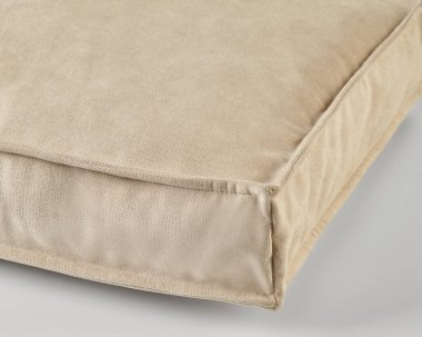 Yumuşak, kare bej kadife yastık düz bir arka planda, dokusu ve işçiliği vurguluyor.