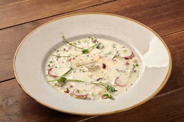 Geleneksel Rus soğuk çorbası kefir, sebze, bitki ve baharatla ahşap masada servis edilen beyaz tabakta.