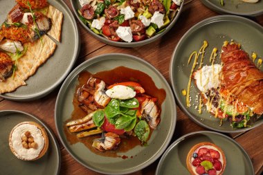 Ahşap masada sergilenen restoran menüleri: füme yılan balığı, salata, kruvasan sandviçi ve tatlı.