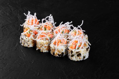 Uramaki suşisi somon, salatalık, çıtır çıtır soslu ve susamlı, siyah arka planda servis edilir.