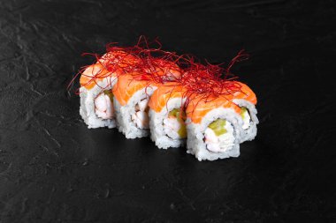 Somon, karides, avokado, krem peynir ve siyah arka planda duran kırmızı baharatlı lezzetli uramaki suşisi.