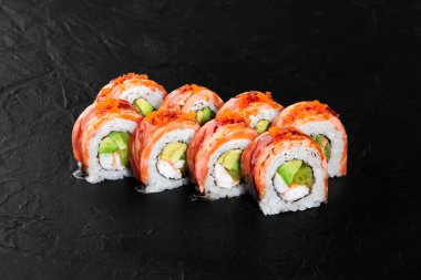 Somon, avokado ve tobiko içeren taze hazırlanmış suşi dürümleri. Siyah arka planda güzelce yerleştirilmiş.