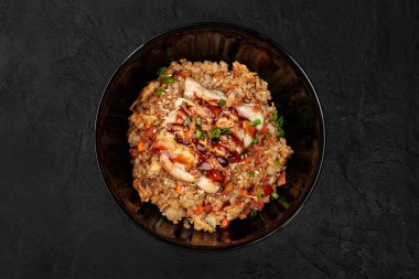 Wok-style teriyaki tavuğu, pilav, sebze ve susam tohumlu, siyah bir kase içinde koyu bir arka planda.