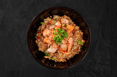 Taze soğan ve susam tohumlarıyla süslenmiş lezzetli somon kızartmalı pilav servisi, şık bir siyah kasede servis ediliyor.