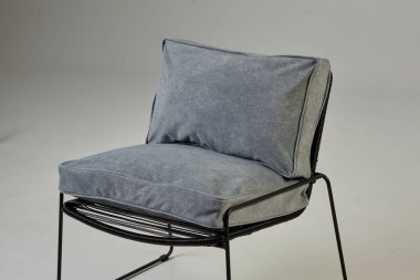 Boş bir odada duran siyah metal çerçeveli rahat gri tekstil koltuğu modern iç tasarımı temsil ediyor.