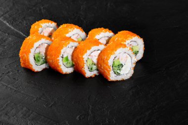 Lezzetli taze California uramaki suşisi karides, avokado, salatalık, krem peynir ve siyah bir tabakta tobiko.