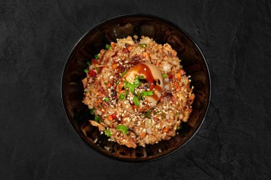 Yumurtalı kızarmış pirinç, susam tohumu, yeşil soğan ve soya sosu, siyah bir kasede servis edilir.